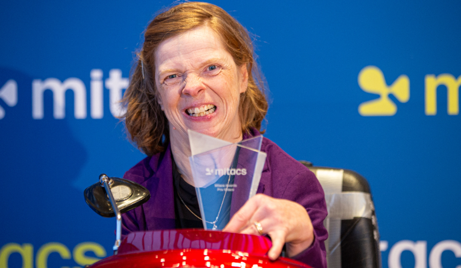A woman in a motorized chair smiles with a glass award.